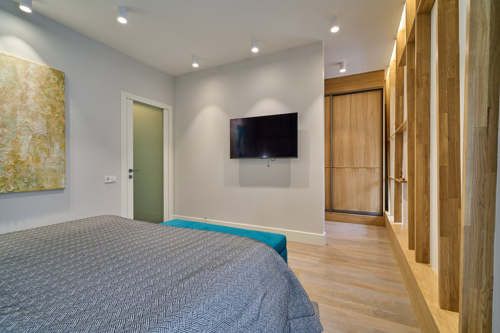 Интерьер спальни с керамогранитом на стену с телевизором, рейками с подсветкой, подсветкой настенной и подсветкой светодиодной в современном стиле